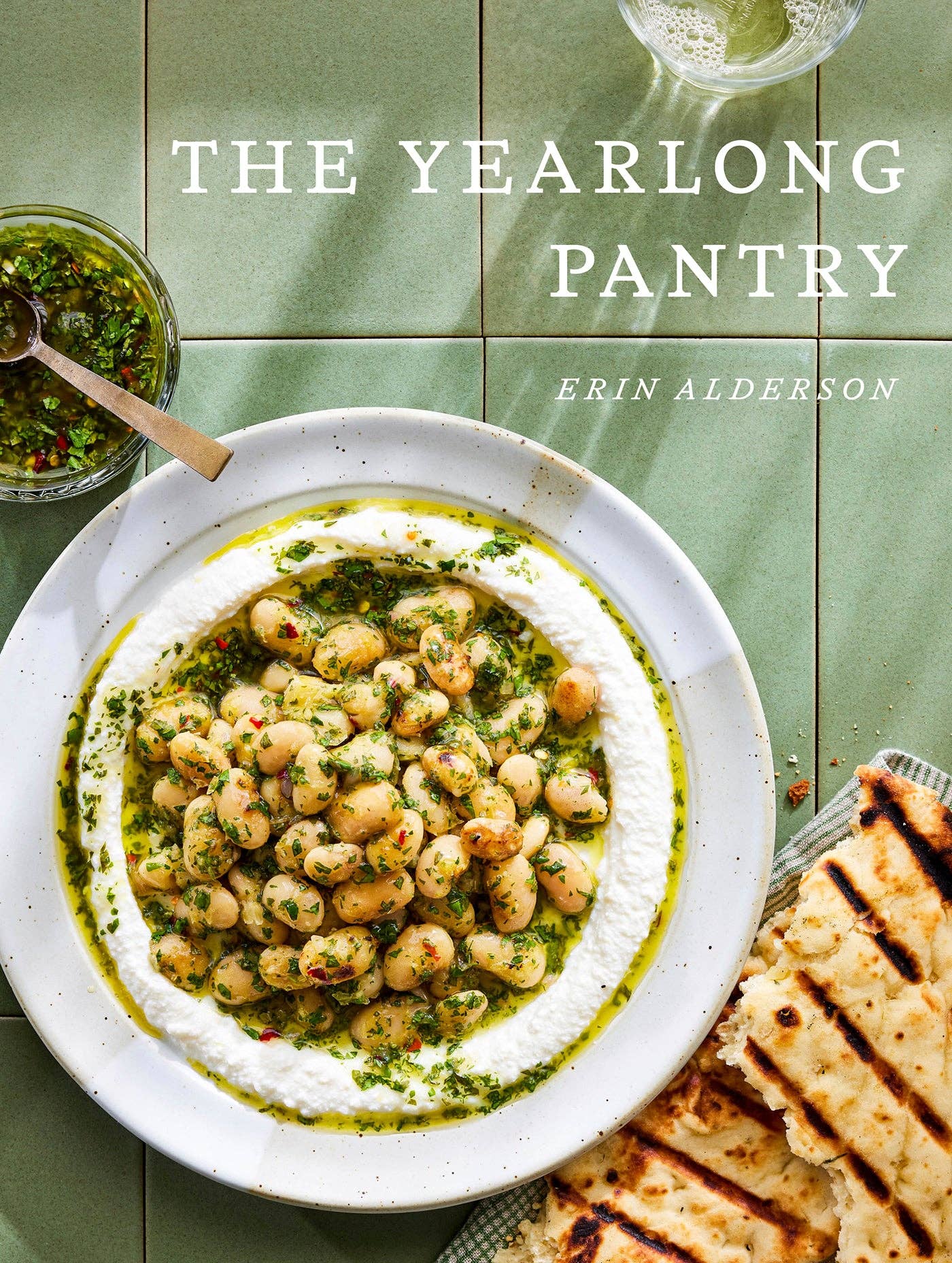 Book cover of 'The Yearlong Pantry' with a dish of chickpeas and herbs on a green tiled background.