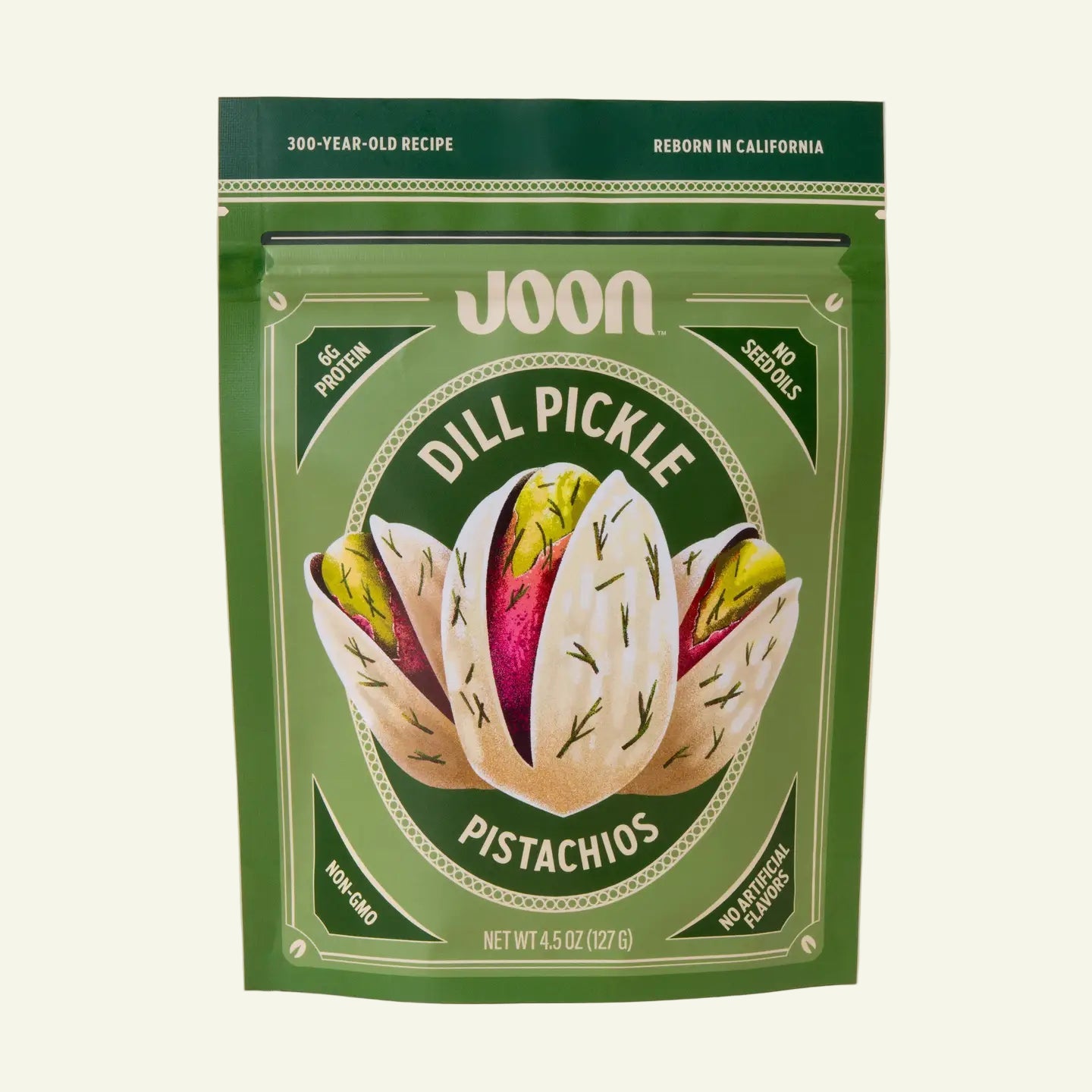 Green package of Joon Dill Pickle Pistachios on a light pink background
