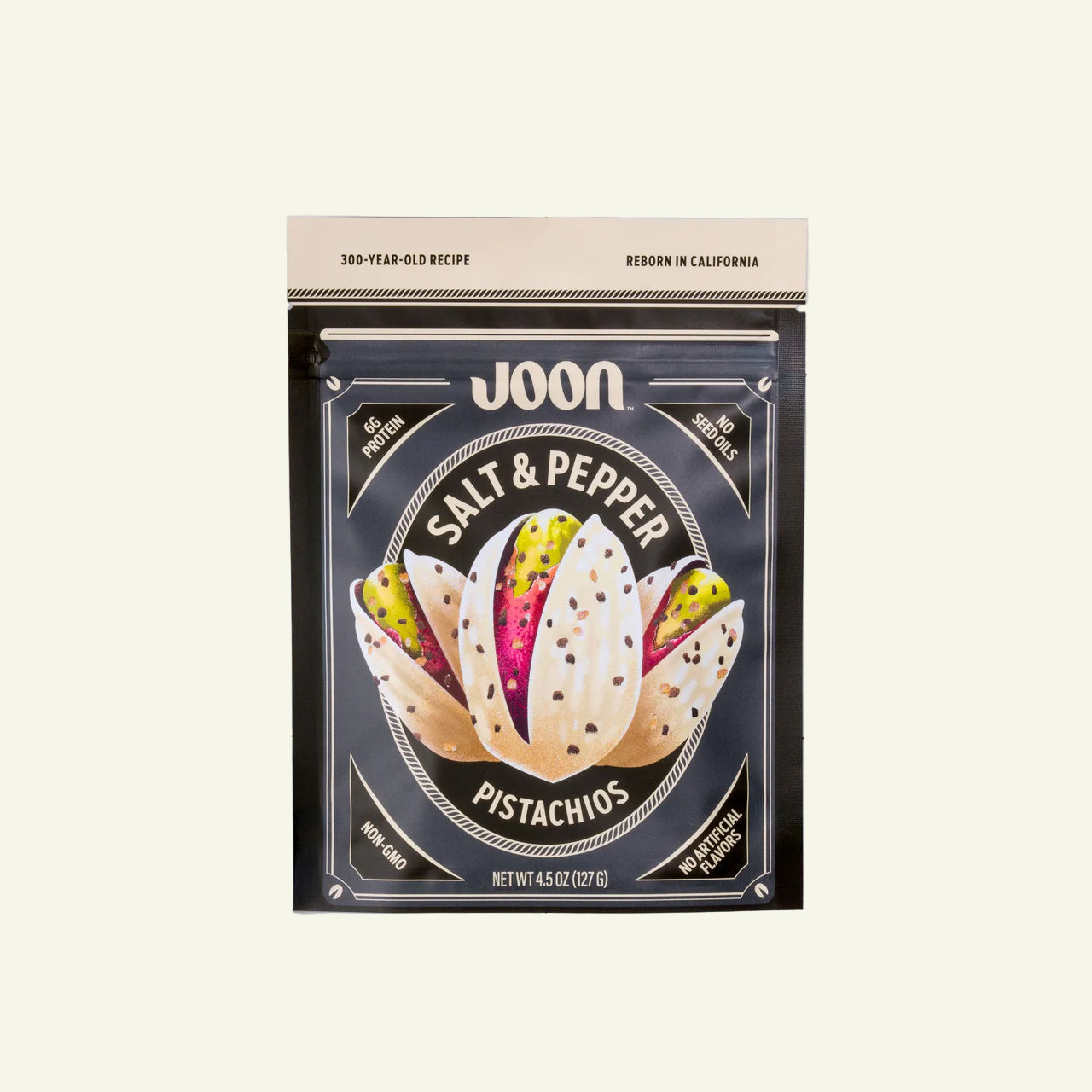 Packaging of Joon Salt & Pepper Pistachios on a white tiled surface with pistachios scattered around.