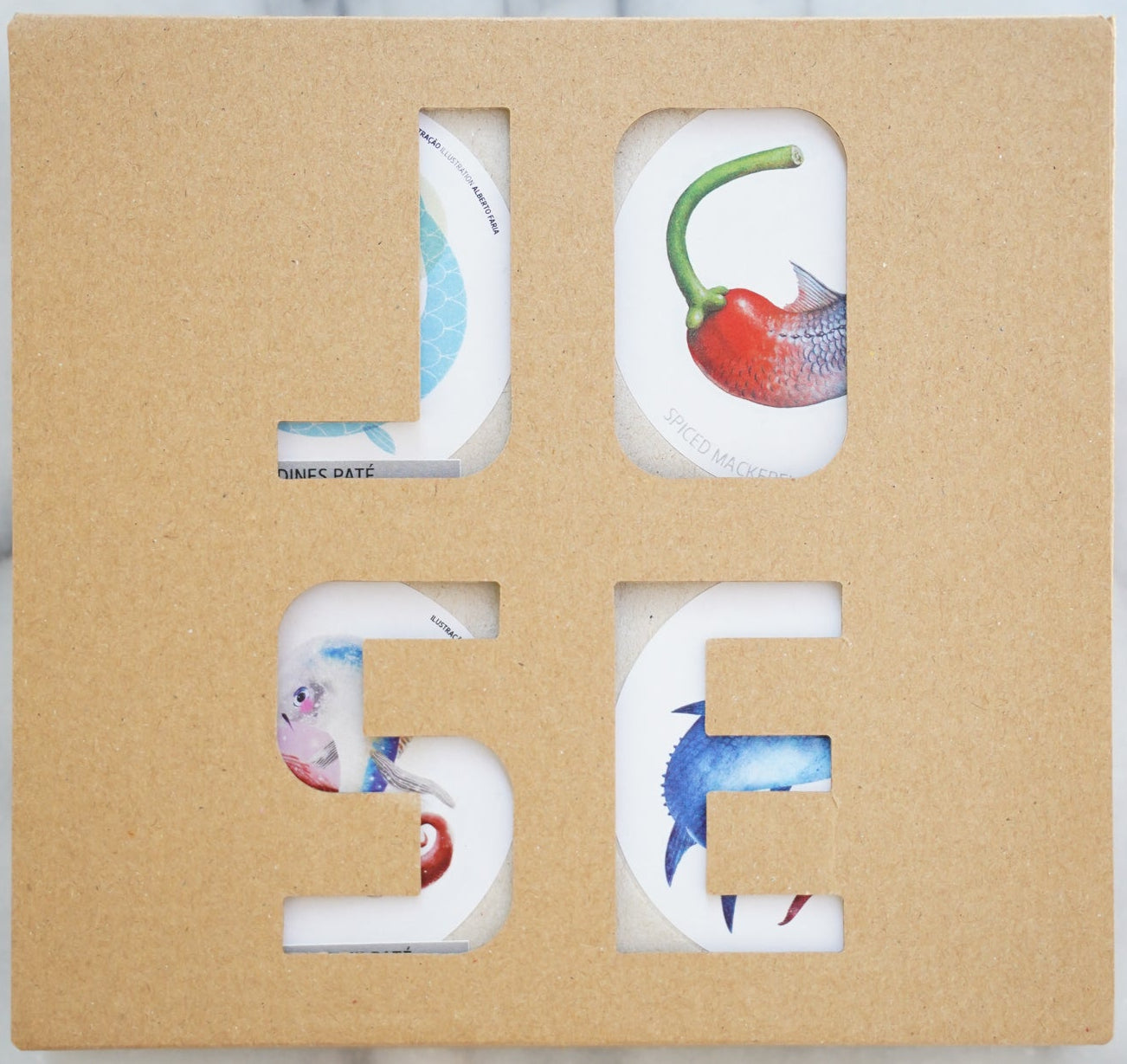 Letter-shaped coasters with colorful designs in a cardboard holder on a marble surface