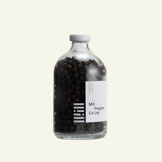 Glass bottle filled with black peppercorns on a white background
