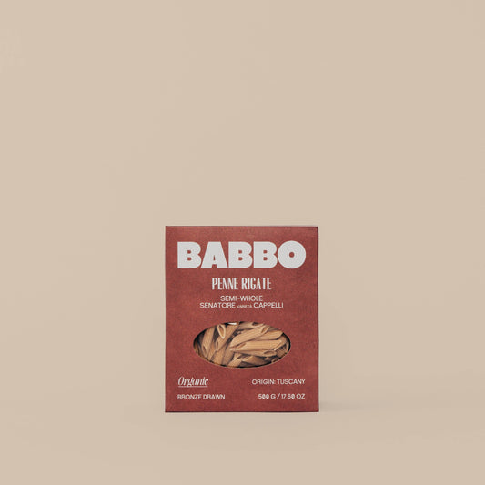 A package of Babbo brand Semi-Whole Grain Penne pasta made from Senatore Cappelli wheat, with a visible window showing the dried pasta inside.