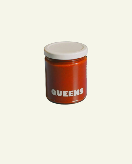 Jar of honey labeled 'QUEENS' on a light surface with a blurred background